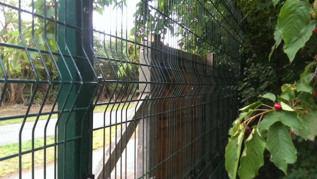 Large green metal fence installed behind wooden fence between Downhams Lane and Alice Bell Close, Cambridge